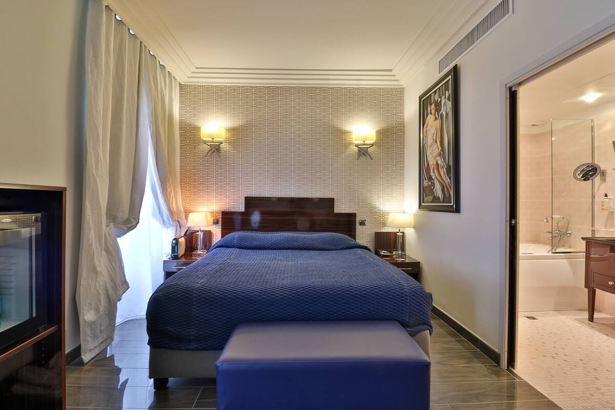 Une chambre d’hôtel avec un grand lit, une télévision, un bureau et une salle de bain équipée d’une baignoire et d’une douche.