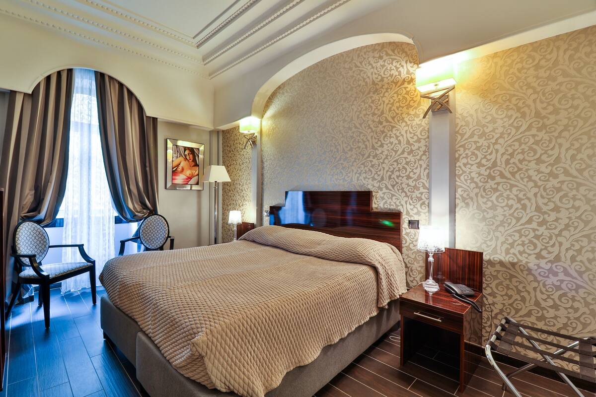 Une chambre d’hôtel avec un grand lit, un bureau avec une lampe, une chaise et un téléviseur fixé au mur.