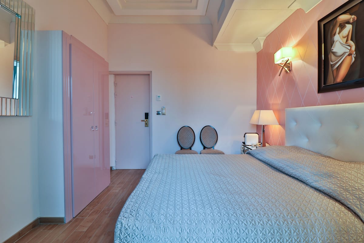 Une chambre à coucher avec un lit, deux chaises, une table de chevet, une lampe et un tableau au mur.