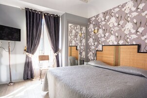 Et hotelværelse med en seng, gardiner, et fjernsyn og en væg med blomstermønster.
