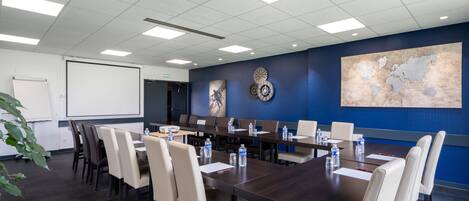 A conference room with a large table, multiple chairs, a projector screen, and a world map on the wall.