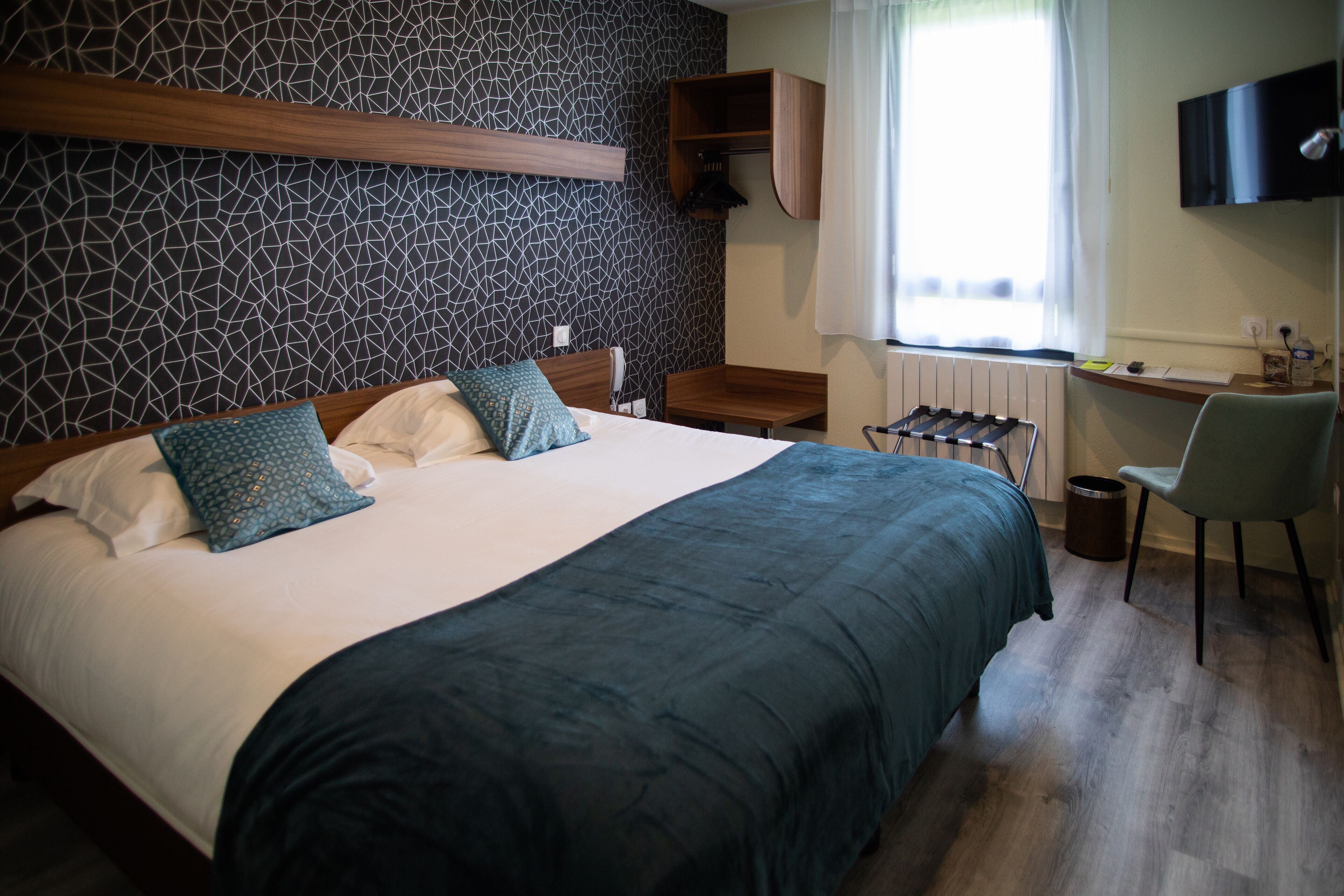 A hotel room with a large bed, a desk, a chair, a TV, and a radiator.