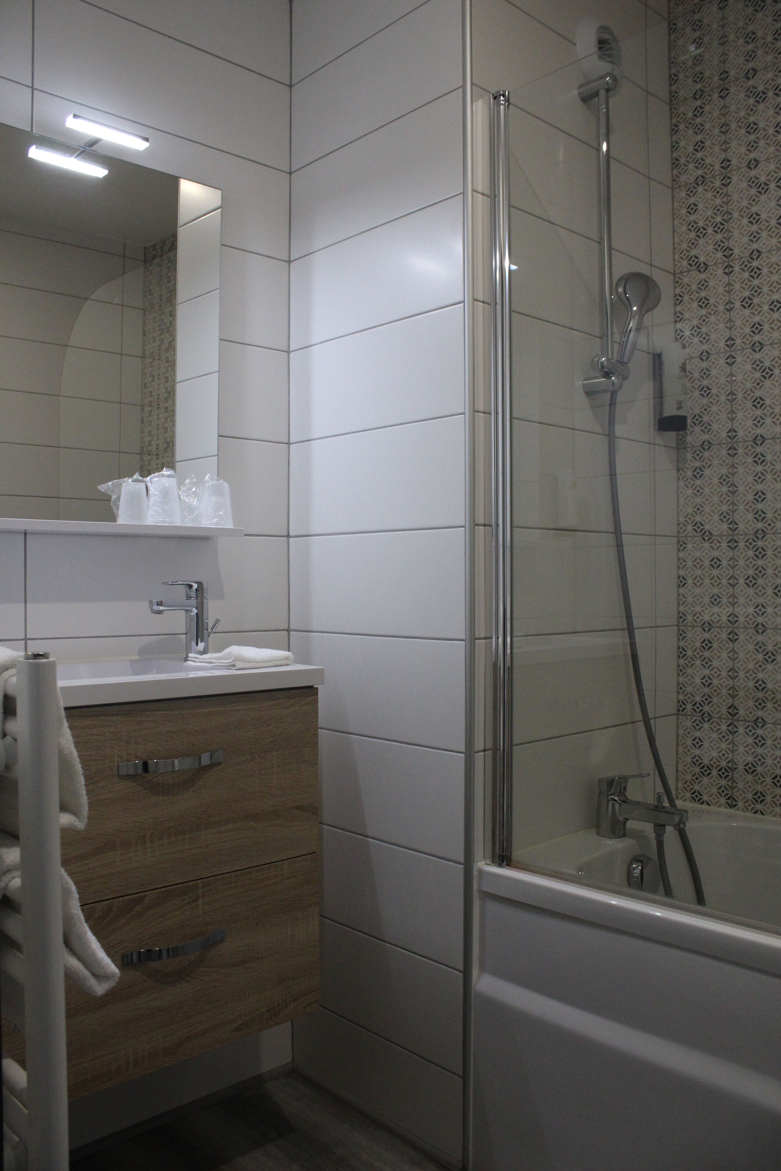 Ein Badezimmer mit einer gläsernen Duschkabine, einem hölzernen Waschtisch mit Spiegel und einer gefliesten Wand.
