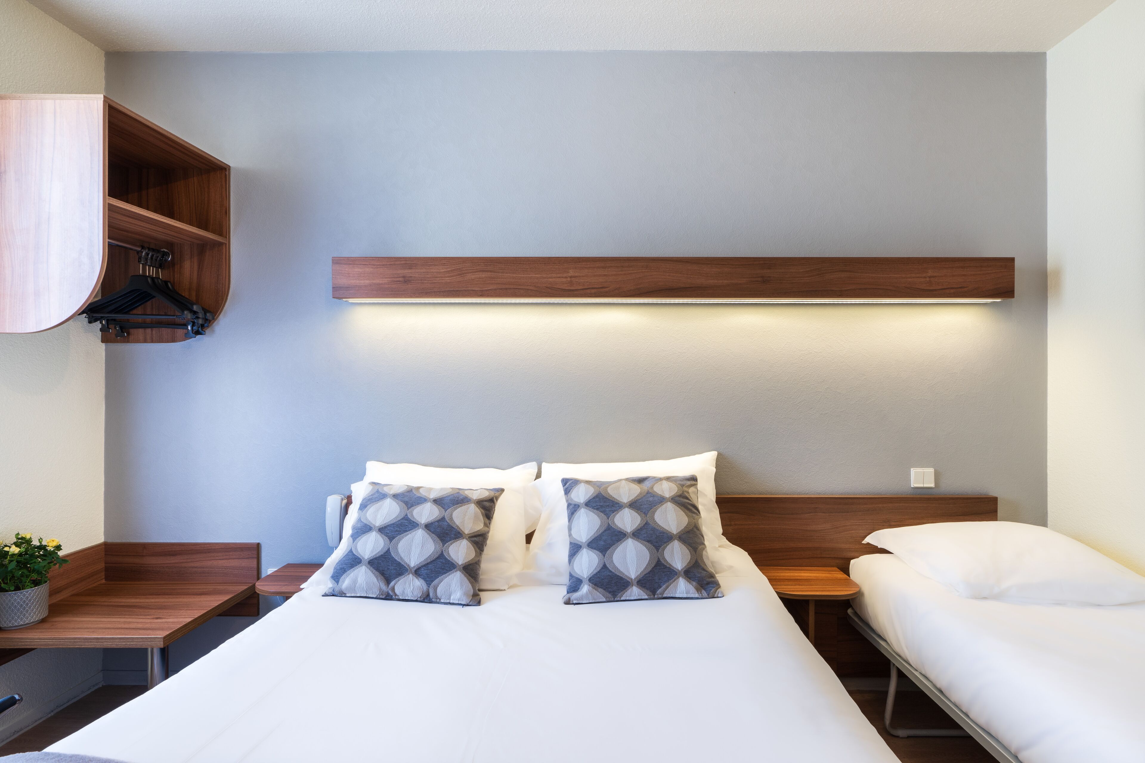 A hotel room with a bed, bedside tables, a wooden shelf, and a hanging light fixture.