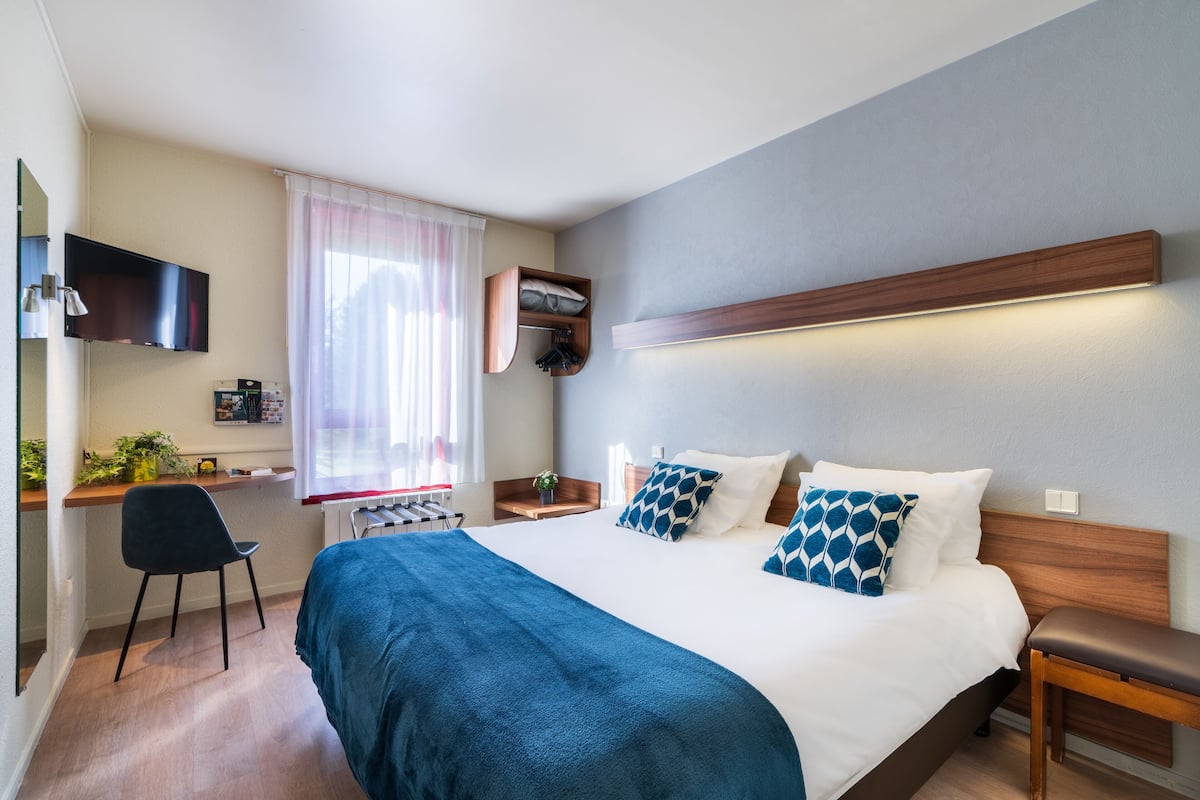 Une chambre d’hôtel avec un lit, un bureau, une chaise et un téléviseur.