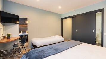 A modern hotel room with a desk, two single beds, a chair, and a large mirror.