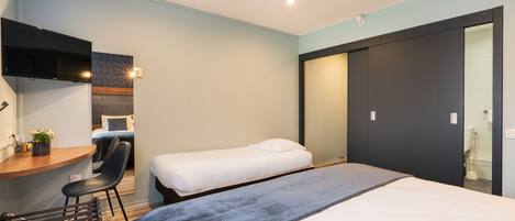 Una habitación de hotel moderna con un escritorio, dos camas individuales, una silla y un espejo grande.