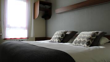 A neatly made bed with a dark blanket and patterned pillows, a wooden headboard, and a built-in shelf above the bed.