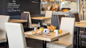 A breakfast setting with a table set for two, including croissants, orange juice, and a coffee cup.