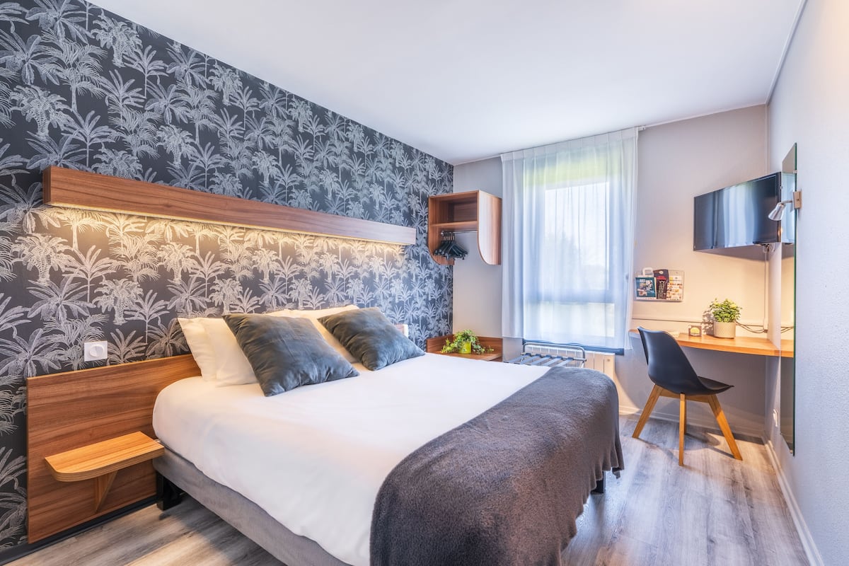 Une chambre d’hôtel moderne, dotée d’un grand lit, d’un bureau avec une chaise, d’une télévision et d’une fenêtre avec des rideaux.