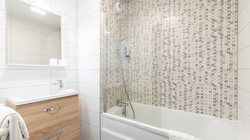 A bathroom with a white sink, wooden cabinet, and a glass-enclosed shower.