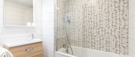 Un baño con lavamanos blanco, mueble de madera y ducha con mampara de vidrio.
