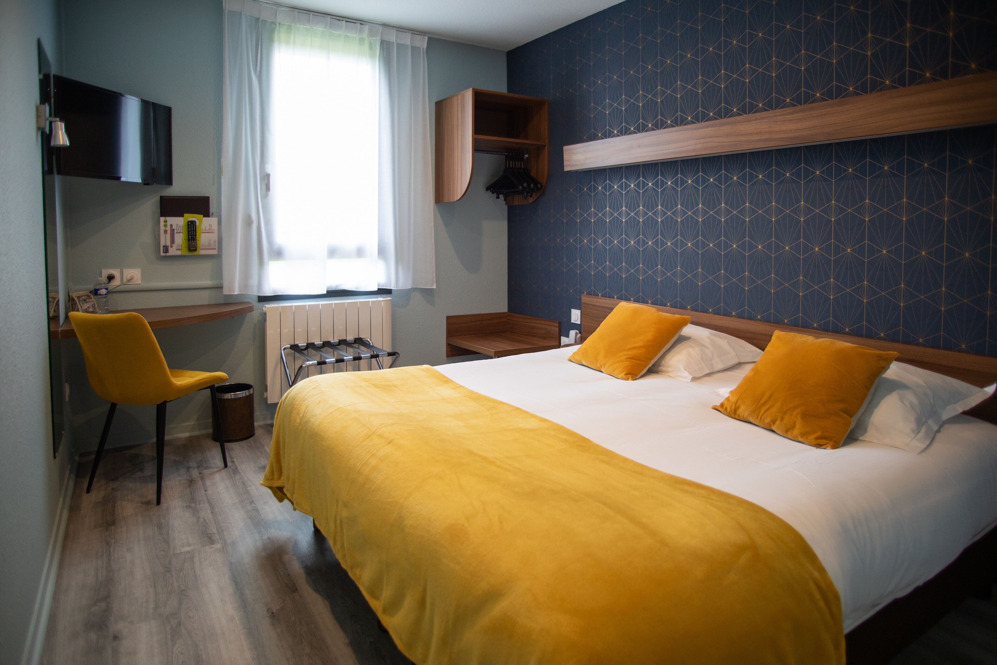 A hotel room with a bed, a desk, a chair, and a window with curtains.