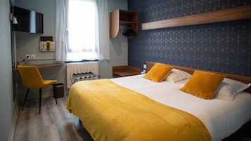 A hotel room with a bed, a desk, a chair, and a window with curtains.