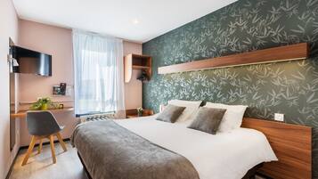 A modern hotel room with a large bed, a desk, and a TV.