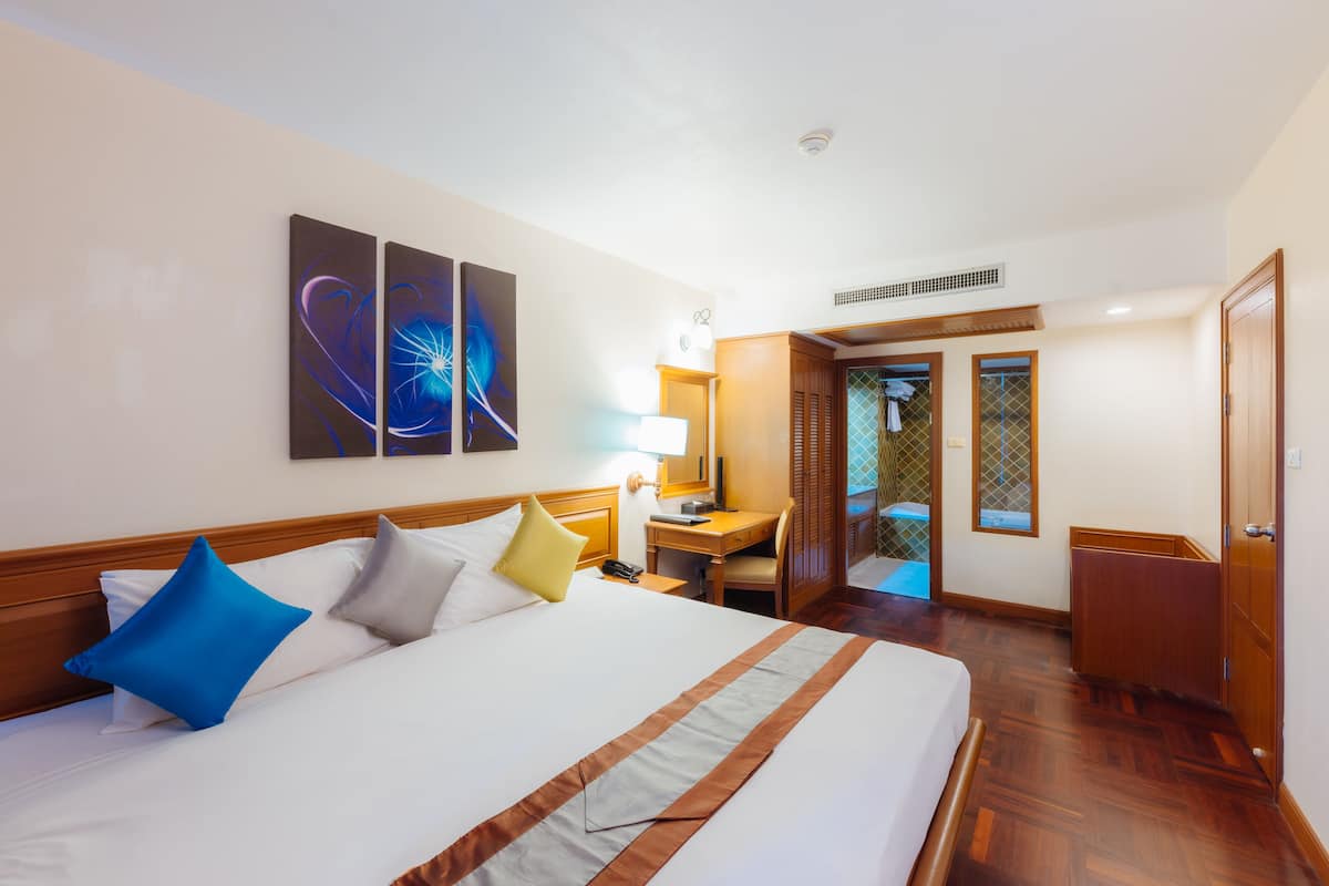 A hotel room with a large bed, a desk, a chair, and a wardrobe.