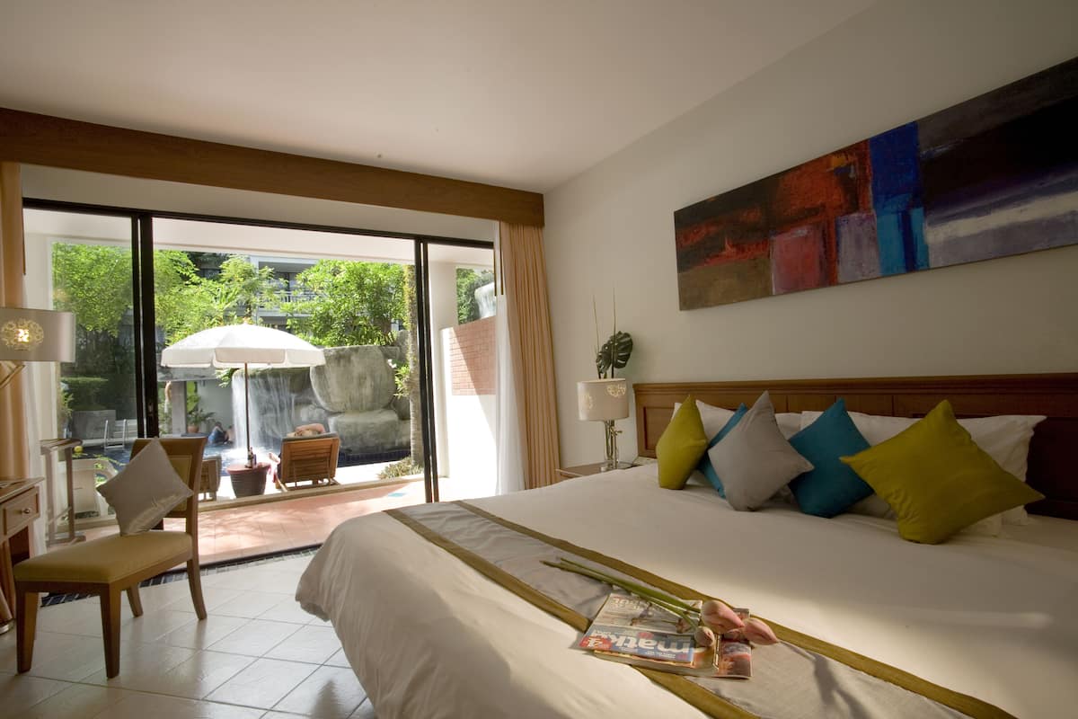 A hotel room with a large bed, a view of a pool and outdoor area, and a painting on the wall.