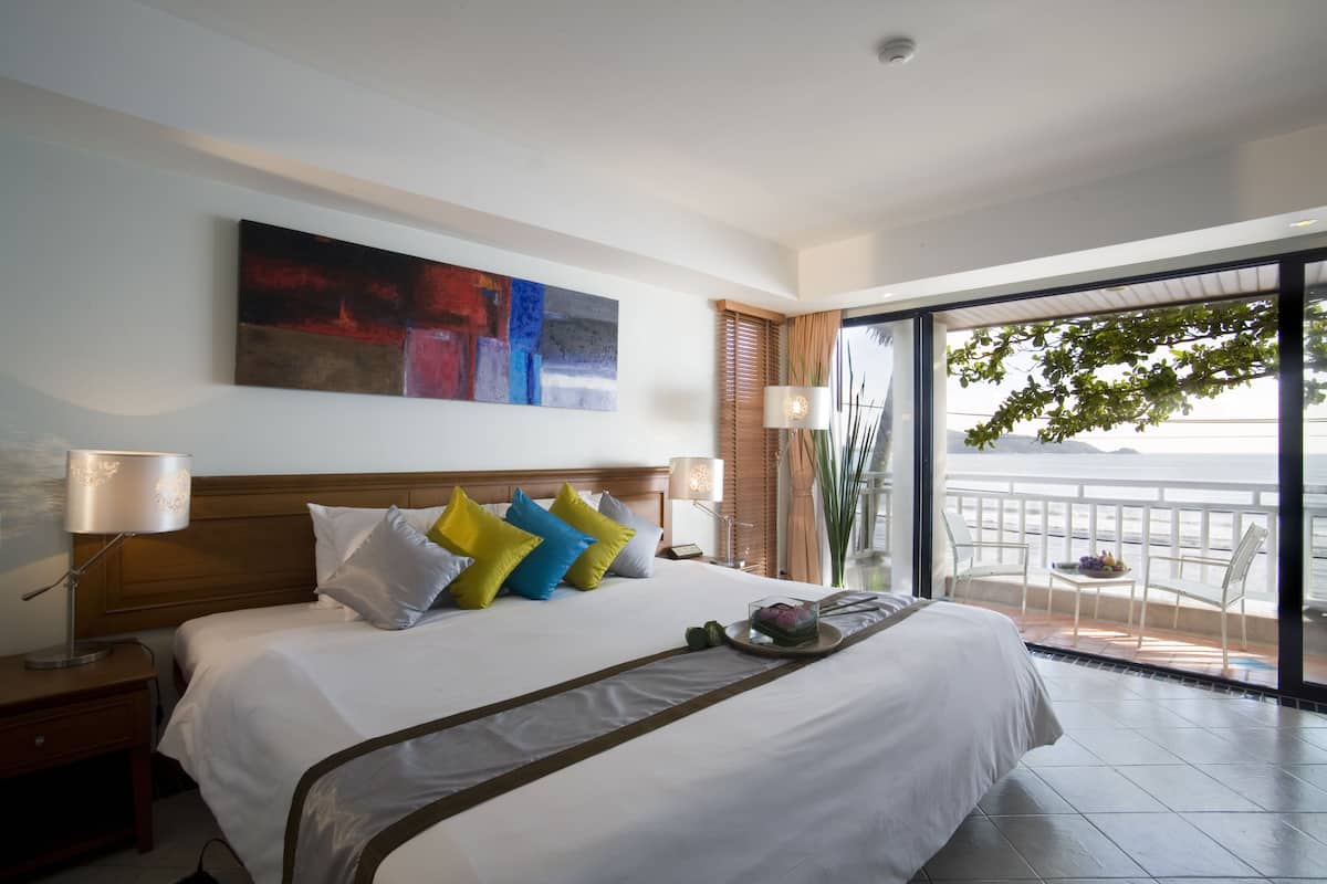 A hotel room with a large bed, a painting on the wall, and a balcony with a view.