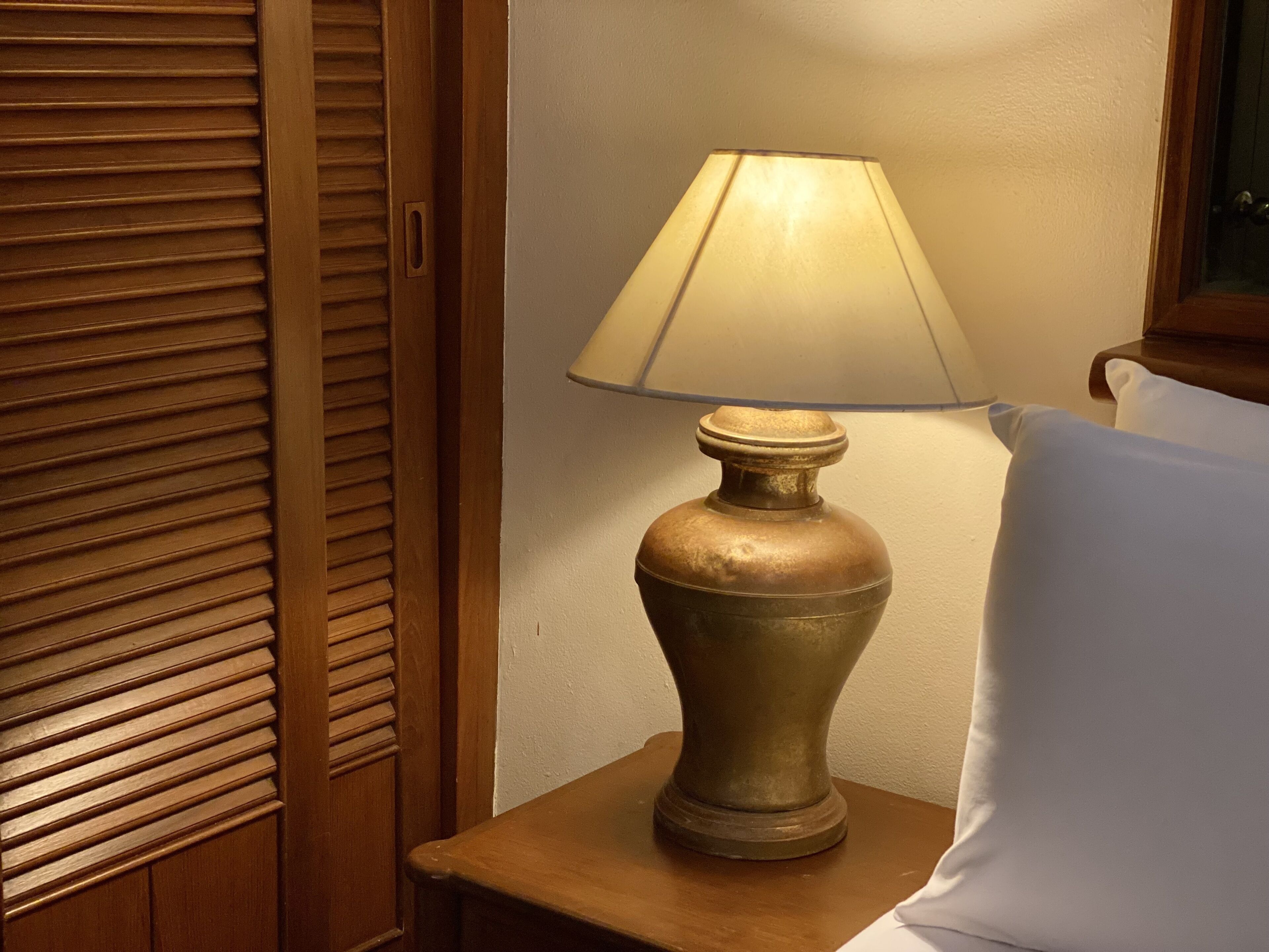 Une table de chevet en bois, une lampe en laiton et un coussin blanc.
