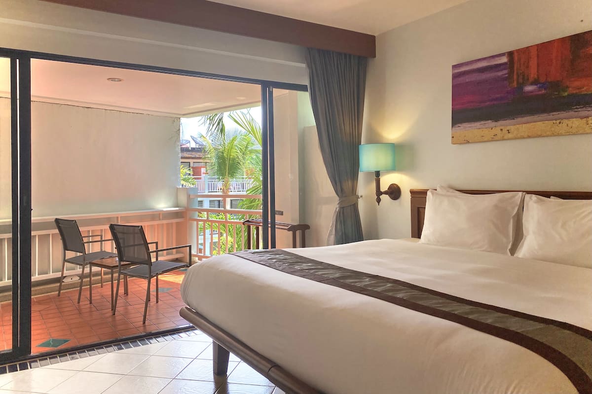 A hotel room with a large bed, a balcony with chairs, and a painting on the wall.