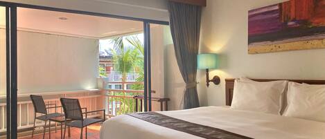 A hotel room with a large bed, a balcony with chairs, and a painting on the wall.