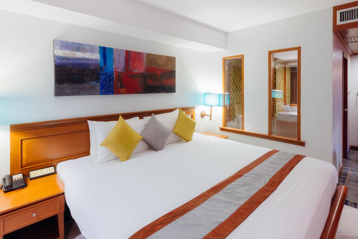 A hotel room with a large bed, a bedside table with a phone, a wall-mounted artwork, and a window with a view.