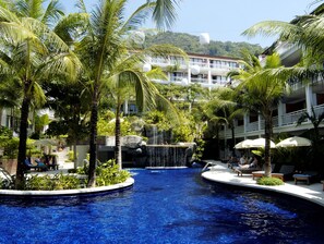 Uma área de piscina com cachoeira, palmeiras e espreguiçadeiras.