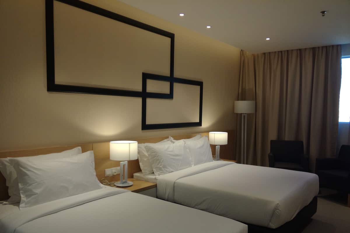 A hotel room with two beds, a desk, a chair, and a large window with curtains.