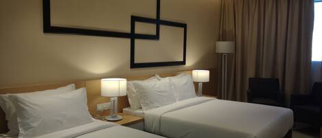 Habitación de hotel con dos camas, un escritorio, una silla y un ventanal con cortinas.