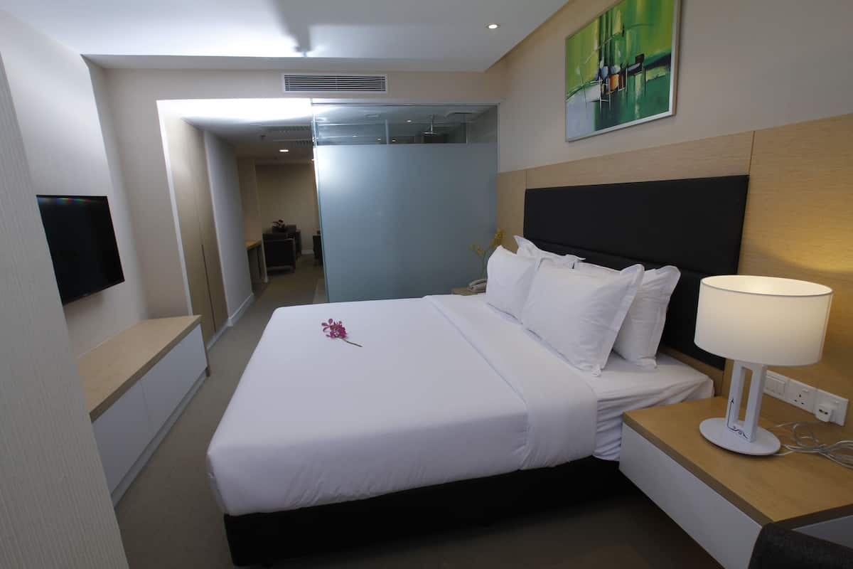 A hotel room with a bed, a bedside table with a lamp, a TV on the wall, and a painting above the bed.