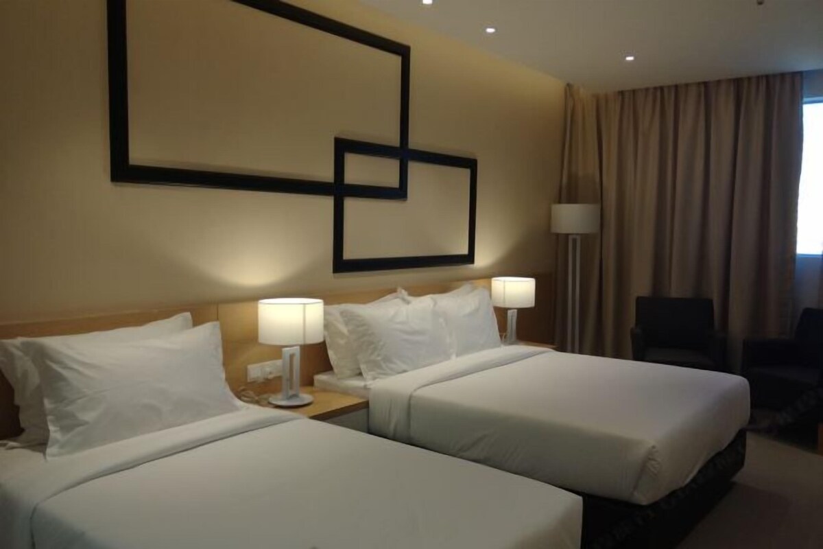A hotel room with two beds, a nightstand with lamps, a large abstract wall decoration, and a view of the outside through a window with curtains.