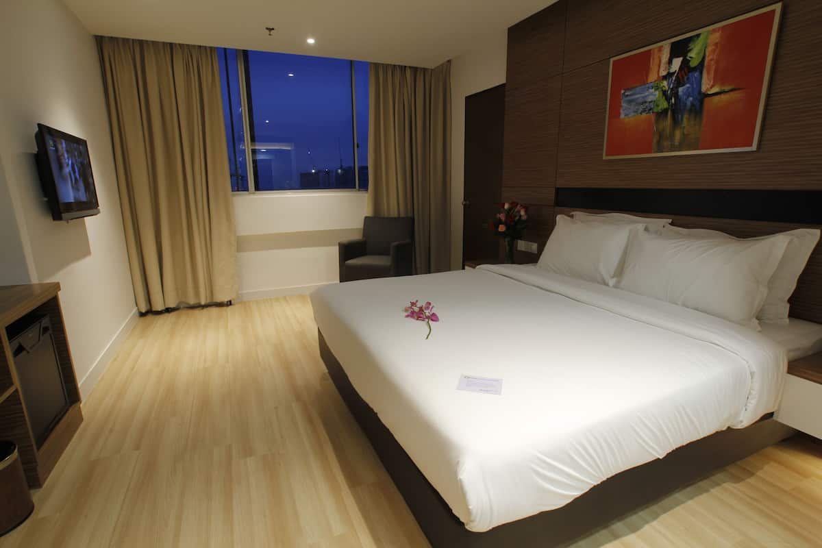 A hotel room with a large bed, a TV mounted on the wall, and a window with curtains.