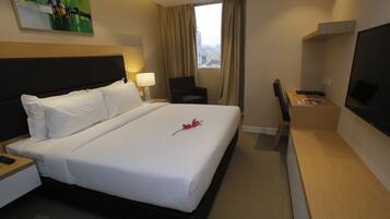 A hotel room with a large bed, a desk with a computer, a chair, a TV, and a window with curtains.