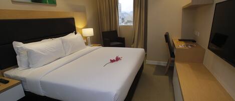Una habitación de hotel con una cama grande, un escritorio con computadora, una silla, un televisor y una ventana con cortinas.