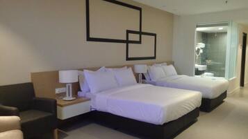 Een moderne hotelkamer met twee bedden, een bank, een nachtkastje en een zichtbare badkamer door een glazen deur.