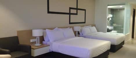 A modern hotel room with two beds, a sofa, a nightstand, and a bathroom visible through a glass door.