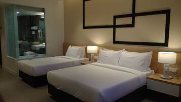 A hotel room with two beds, a bathroom with a glass partition, and a wall-mounted artwork.