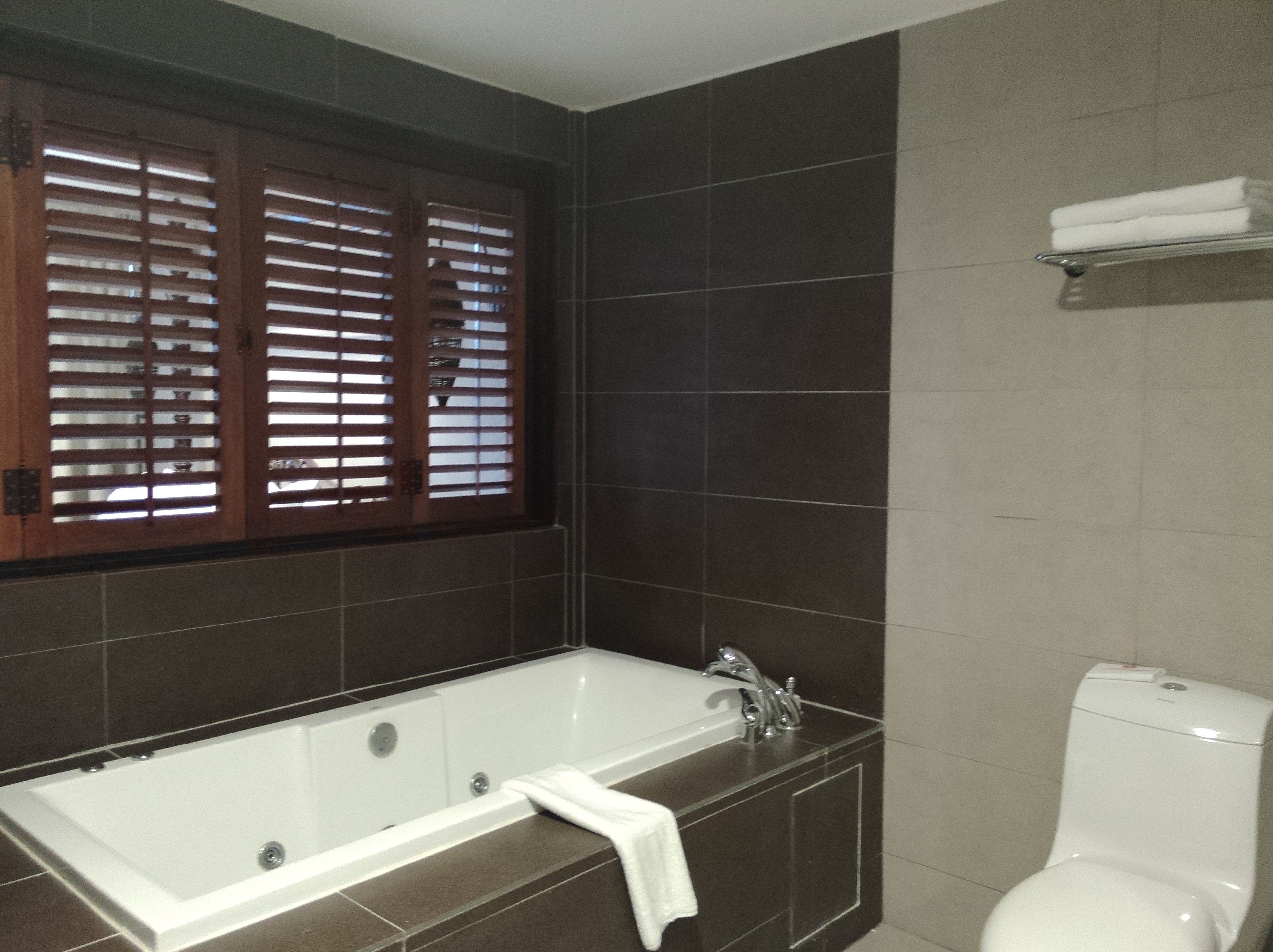 Un baño con bañera, inodoro y ventana con persianas.