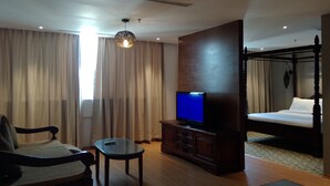 Habitació d'hotel amb un llit, una televisió, un armari de fusta, una cadira i una làmpada penjant.