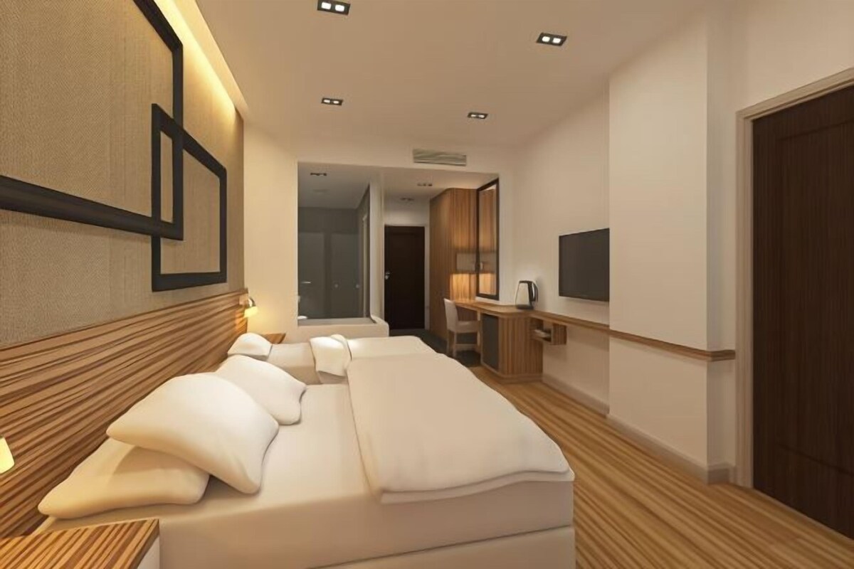 Una habitación de hotel moderna con una cama grande, mesitas de noche, un escritorio y una televisión.