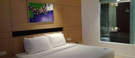 Una habitación de hotel moderna con una cama grande, una mesita de noche, un cuadro colgado en la pared y un ventanal con vistas al interior.