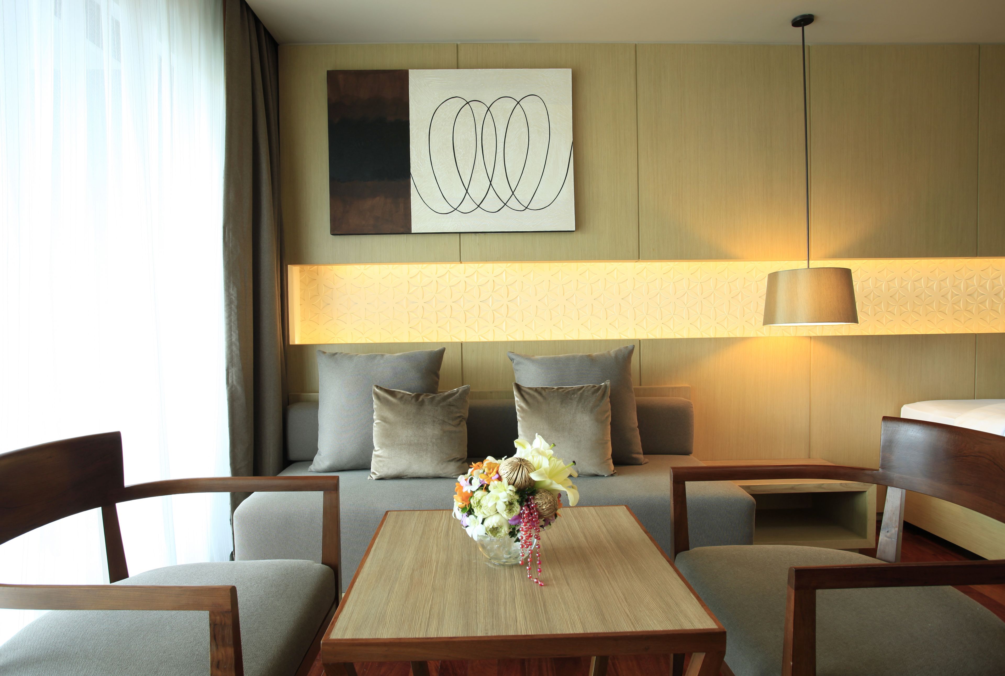 Habitació d'hotel amb un sofà, dues butaques, una taula de fusta i una obra d'art abstracta penjada a la paret.
