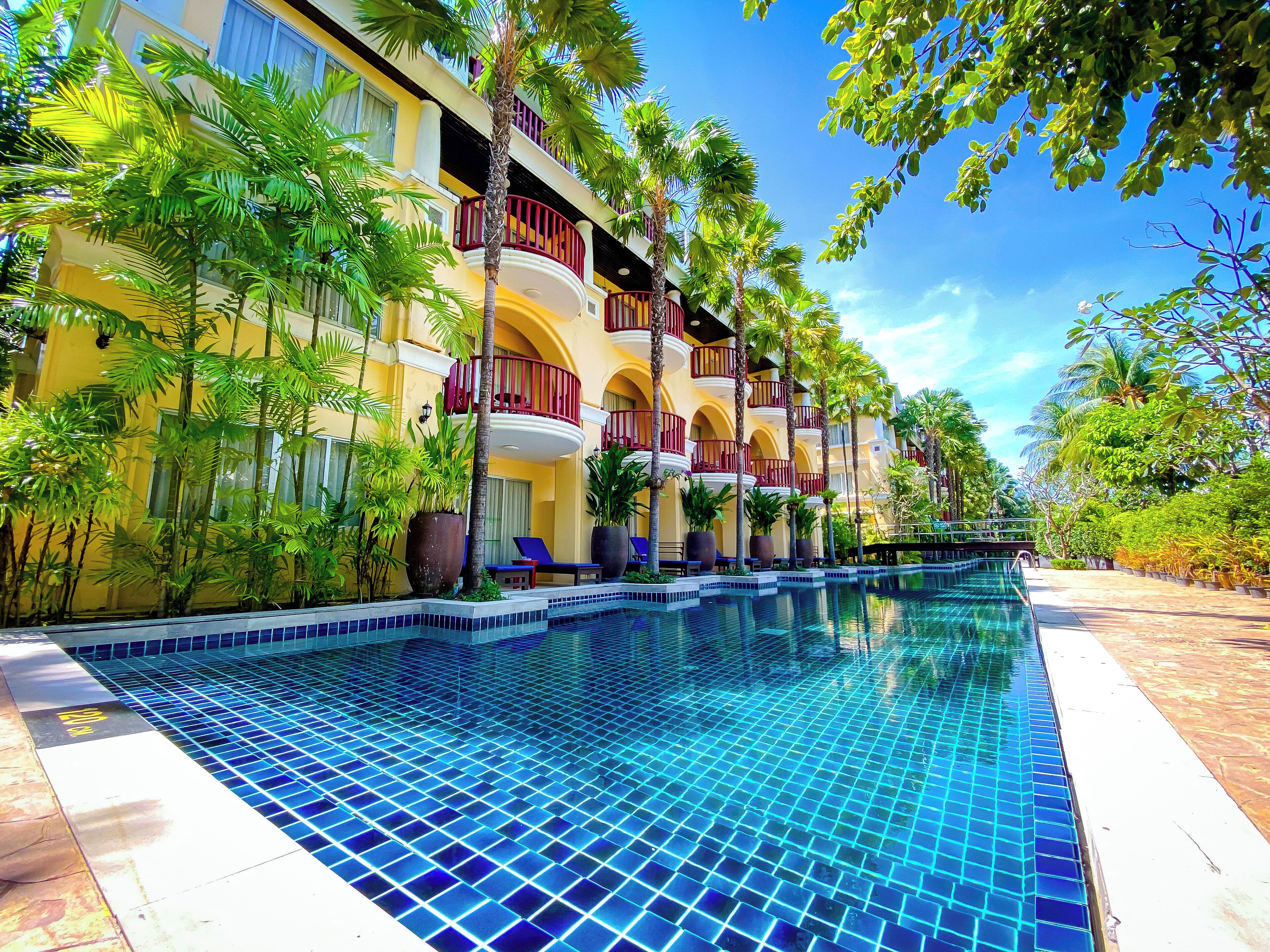 Un hotel con piscina, varios balcones y abundante vegetación.