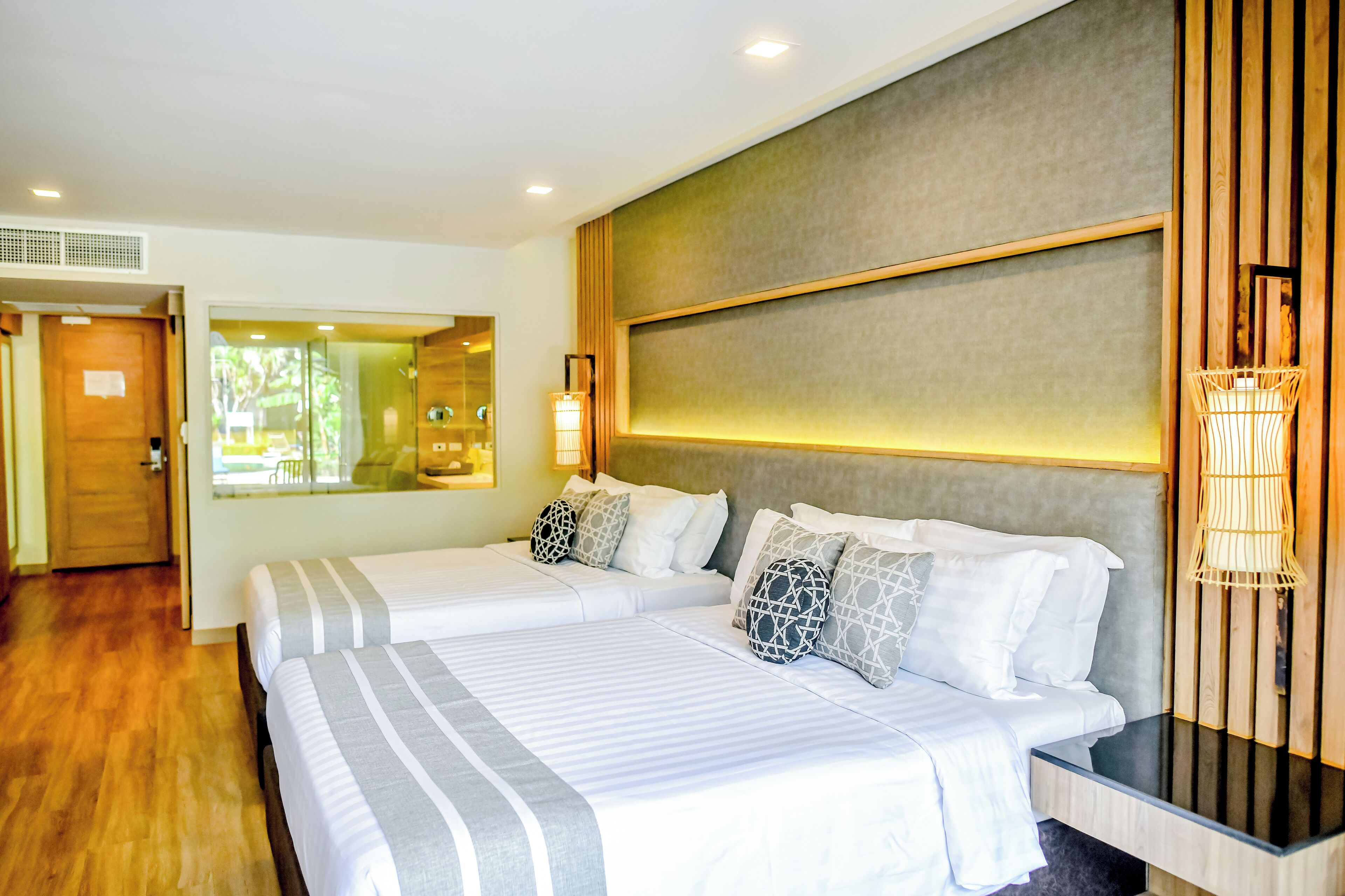 Habitación de hotel con dos camas, piso de madera, un ventanal con vistas y una lámpara fijada a la pared.