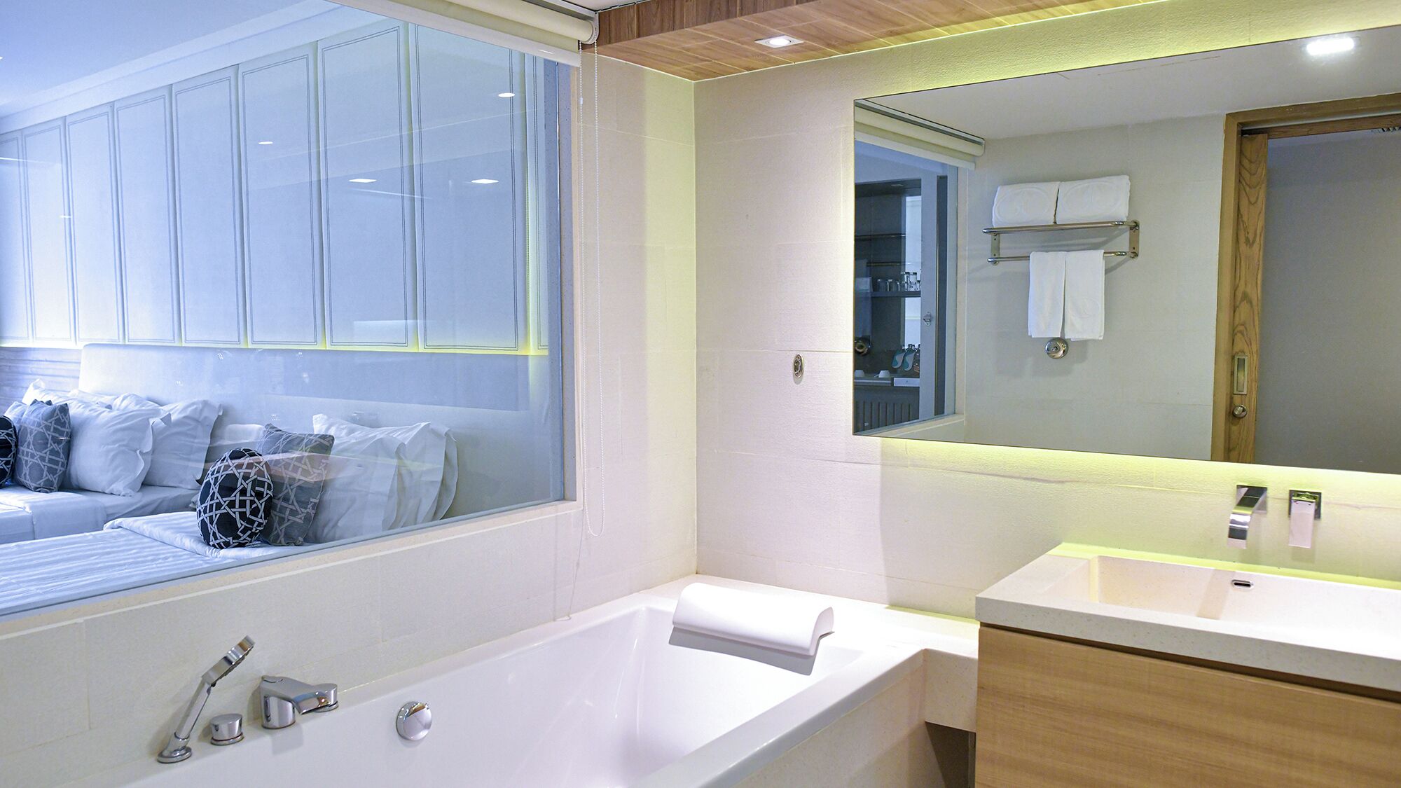 A modern bathroom with a large window, a bathtub, a vanity with a mirror, and a wooden ceiling.