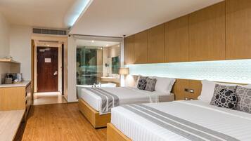 A hotel room with two beds, a wooden headboard, a glass shower enclosure, and a small desk with a coffee machine.
