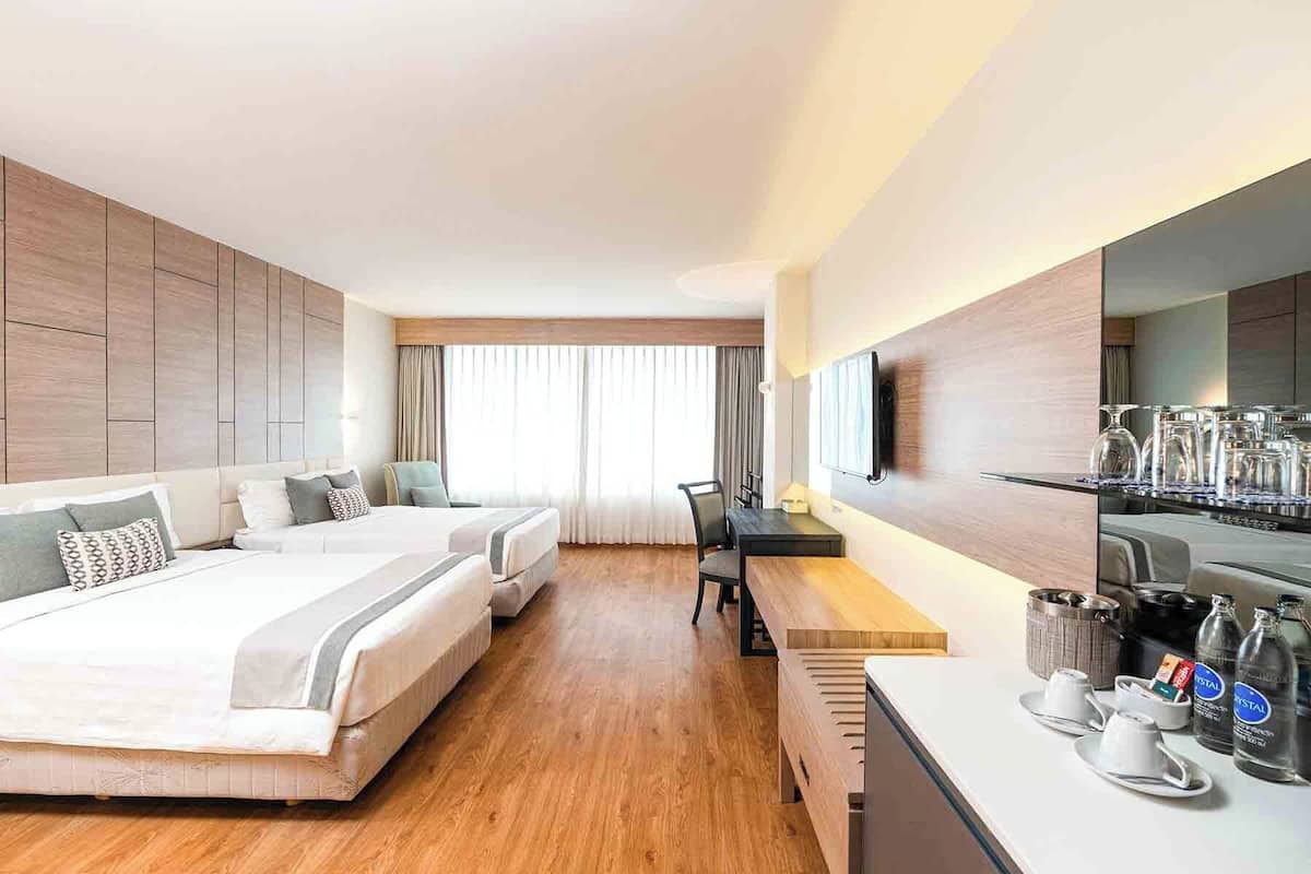A hotel room with two beds, a desk, a chair, a TV, and a minibar.