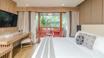 Una habitación de hotel con cama, escritorio, televisor y balcón con sillas rojas.