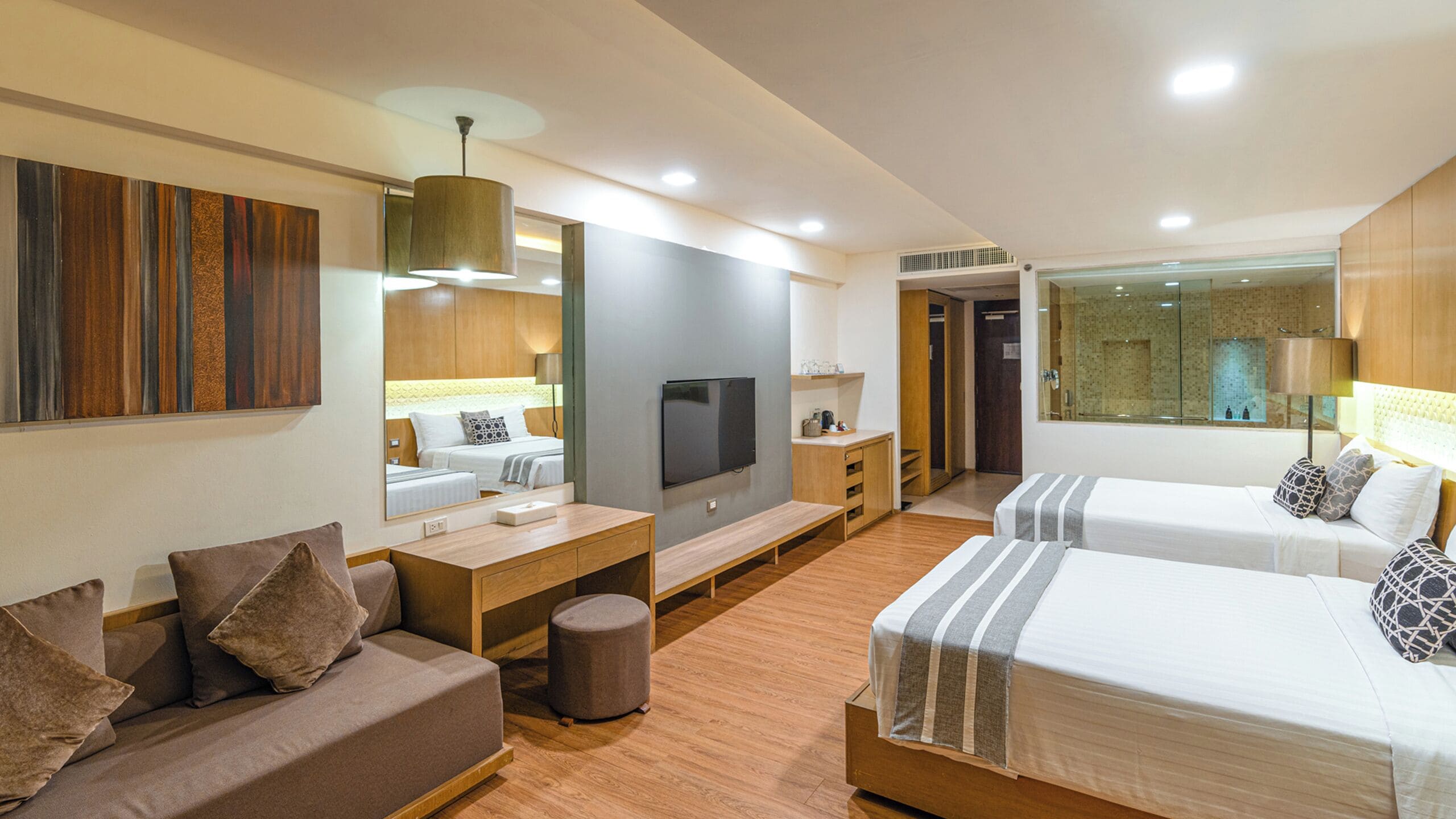 A modern hotel room with a sofa, two single beds, a TV, a desk, and a mirror.