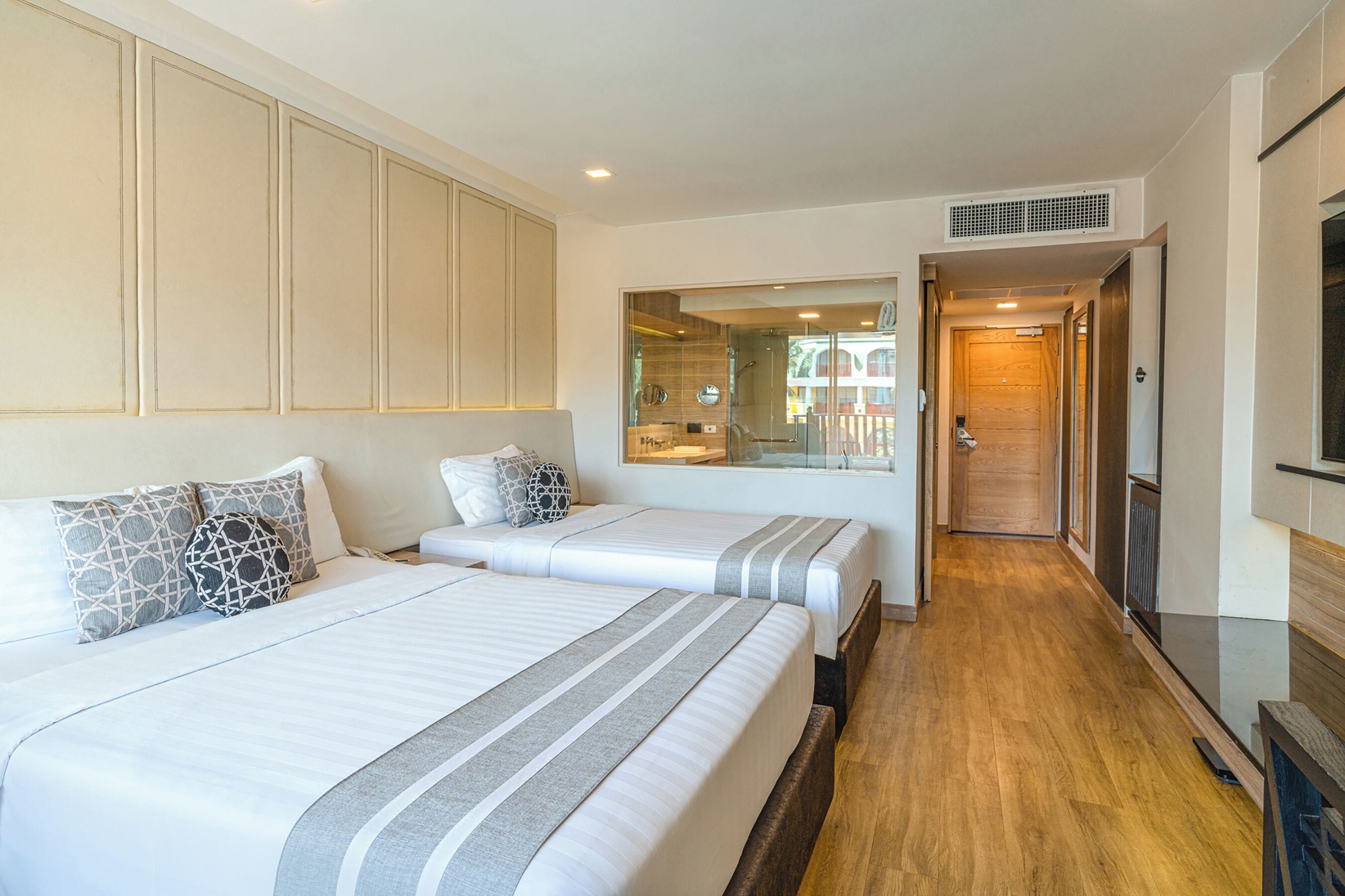 Habitación de hotel con dos camas, un espejo grande, suelo de madera y vista a la calle a través de un ventanal.